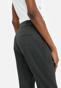 Pantaloni sagomati grigio scuro con una texture liscia, vestibilità slim e tasche posteriori sottili. La vita è piatta e il tessuto appare leggermente texturizzato.
