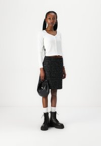 Haut blanc à manches longues, jupe noire texturée avec des accents métalliques, associée à des bottes plateformes noires et un sac à main noir.