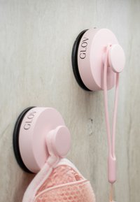 Ganci a ventosa rosa con basi circolari e accenti neri, che sorreggono un morbido tessuto rosa testurizzato, montati su una parete di colore chiaro.