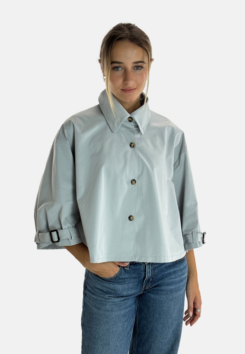 Lys grå cropped jakke med høj krave, store knapper og manchetter med stropper og spænder. Glat, let stof, minimalistisk design.