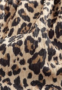 Leopardikuvioinen kangas, jossa on tekstuurimaista pintaa beige, musta ja ruskea sävyissä. Kankaassa on epäsäännöllisiä läiskiä ja pehmeä, virtaava ulkonäkö.