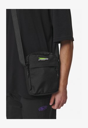 Zwarte schoudertas van gestructureerde stof, verstelbare schouderband, ritsvak en een klein groen logo aan de voorkant. Compact en functioneel ontwerp.