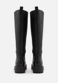 Schwarze knöchelhohe Stiefel aus glattem Leder, mit einer robusten Gummisohle und einer Schlaufe an der Rückseite. Sichtbare Nähte entlang der Nähte.