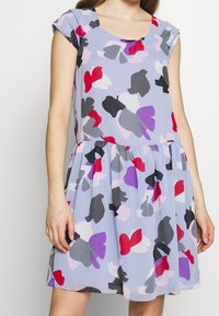 Ärmlös klänning i lätt, texturerad tyg. Har en lavendelfärgad bas med abstrakta blommönster i röd, rosa, svart och lila.