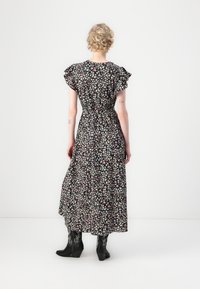 Robe maxi noire à fleurs avec des manches à volants, taille cintrée, présentant des motifs de fleurs roses et blanches. Associée à des bottes à semelles compensées noires.