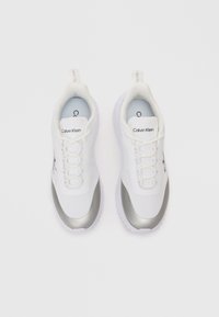 Λευκά αθλητικά παπούτσια με ασημένιες λεπτομέρειες, διαθέτοντας ακατέργαστο άνω μέρος, σχεδίαση με κορδόνια, νάιλον κολάρο και υφασμάτινη σόλα. Ετικέτες στην γλώσσα του παπουτσιού.