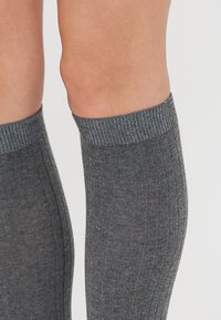 Calze grigie al ginocchio con una texture a coste e una rincalzatura di un grigio scuro a contrasto. Il tessuto sembra morbido e confortevole.