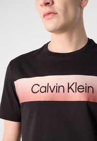 Svart bomulls t-skjorte med en gradient rosa stripe og "Calvin Klein" trykt i svart. Rund hals og korte ermer.