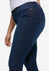 Jeans de mezclilla azul oscuro con corte slim. Incluyen una cintura de talle medio, costuras sutiles y un diseño clásico de cinco bolsillos.