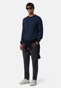 Navyblau gestreifter Pullover, dunkle Hose und helle Sneakers. Pullover um die Taille gebunden, Sonnenbrille und lässiger Schnitt.
