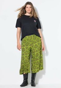 Zwarte T-shirt met een roze hartlogo, gecombineerd met groene wijde broek met een bloemenpatroon. Zwarte cowboylaarzen maken de outfit af.