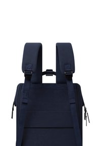 Sac à dos bleu marine avec des bretelles rembourrées, tissu texturé, fermeture éclair latérale et poignée centrale. Design minimaliste avec des bretelles ajustables.