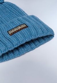 Berretto lavorato a maglia in lana azzurra chiara con una texture a coste, caratterizzato da un'etichetta logata nera e arancione che mostra "NAPAPIJRI geographics."
