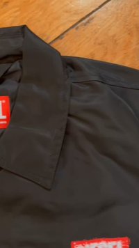 Juodas, lengvas švarkas su tvirtu apykakle. Yra ryškus raudonas dydžio etiketas "L" ir lygus, matinio paviršiaus apdaila. Nėra matomų ornamentų ar detalių.