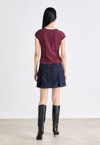 Maroon-färgad åtsittande t-shirt med vit kant, ihop med en mörk denimkjol med veck och svarta knähöga stövlar. Enkelt mönster och perfekt passform.