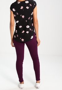 Černá květinová blůza s krátkými rukávy, spárovaná s upnutými fialovými džíny a bílými teniskami. Blůza má růžové a bílé květinové vzory.