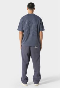 T-shirt surdimensionné gris foncé avec un grand motif ton sur ton dans le dos, associé à un pantalon de survêtement assorti comportant un petit logo sur la poche.