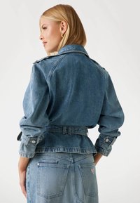 Giubbotto in denim con vita strizzata, maniche lunghe e polsini con bottone. Colore azzurro chiaro con finitura texture e design a peplo.