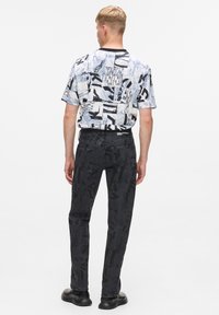 Cămașa cu mânecă scurtă are un model abstract în culorile albastru și alb. Modelul poartă blugi negri cu un design embosat și pantofi negri.