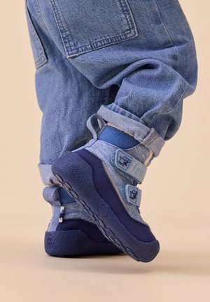Blaue Schuhe mit einer strukturierten Gummisohle, einem oberen Teil aus Stoff in mehreren Blautönen, ausgestattet mit verstellbaren Riemen und Logo-Akzenten.