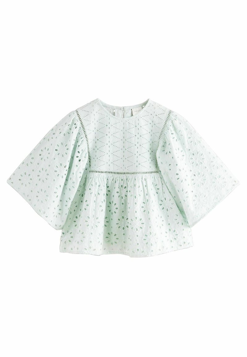 Blouse vert clair avec des manches larges et évasées. Le tissu en broderie présente des découpes florales et des coutures décoratives le long du buste. Encolure ronde.