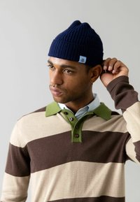 Berretto a coste blu navy e maglione a righe nei toni del beige, marrone e verde. Il maglione presenta un colletto e tre bottoni con un'etichetta di accento blu.