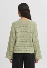 Strickpullover in Hellgrün mit weiten Ärmeln, der strukturierte Streifen und offene Muster aufweist. Die Rückansicht zeigt einen gerippten Hals- und Saumabschluss.