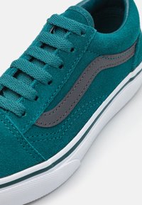 Teal suede sneaker featuring gray leather accents, flat laces, and a white rubber sole with a textured pattern.