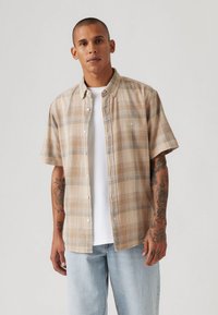 Short-sleeve plaid shirt in tan and beige, featuring a button-down collar, light check pattern, and subtle logo on the chest.