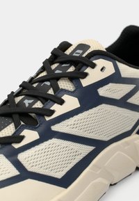 Chaussures de sport présentant une combinaison de tige en mesh crème et de superpositions bleu marine foncé, lacets noirs, semelle profilée et accents texturés.