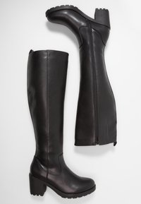 Para czarnych skórzanych kozaków do kolan z blokowym obcasem i bocznymi zamkami błyskawicznymi na białym tle.