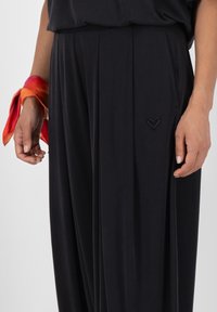 Breda, svarta byxor gjorda av ett mjukt material med subtila veck och en liten hjärtlogotyp på framlommen.