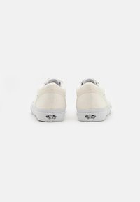 Baskets blanches en toile avec une texture lisse, présentant un design bas et un détail de logo sur le talon. Vue arrière minimaliste.