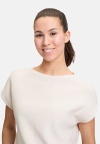 Lys beige kortærmet sweater med en blød, tekstureret overflade og en løs pasform. Har en bred halsudskæring og afrundede skuldersømme.