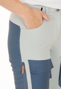 Lichtblauwe en marineblauwe broeken hebben een slim fit, zijzakken en een ritszak met een oranje trekker voor extra functionaliteit.