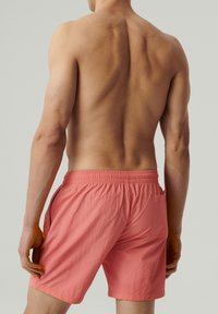 Różowe kąpielówki z elastycznym pasem, tylnią kieszonką oraz lekkim, teksturowanym materiałem. Projekt charakteryzuje się prostym krojem.