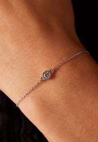 Zilveren schakelsleutelarmband met een enkele ronde heldere steen die in een gestructureerde ronde zetting is geplaatst, getoond op een pols.