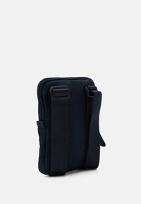 Kompaktní černá crossbody taška s nastavitelnými širokými popruhy a zipovým uzavřením na jednoduch�ém bílém pozadí.