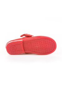 Suela de zapato infantil rojo, mirando hacia arriba, con la talla 25 marcada en el talón, con una textura en el tread y un pequeño lazo en la parte superior.