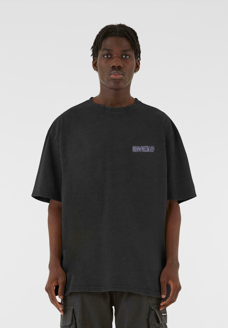 Svart oversized t-skjorte laget av bomull, med korte ermer og rund hals. Små lilla tekstdetaljer på brystet. Glatt tekstur.