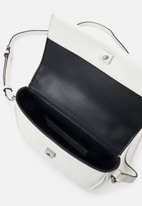 Bolso de mano en blanco y negro con un acabado de cuero suave, diseño plano y un cierre magnético plateado. El interior cuenta con un forro negro y un bolsillo.