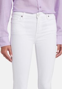 Jeans en denim blanc en coton avec une coupe ajustée, présentant une texture lisse, des poches avant et un bouton de fermeture unique.