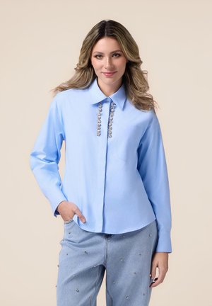 Camicia button-up azzurro chiaro con colletto a punta, decorata nella parte anteriore da dettagli in argento e maniche lunghe. Tessuto morbido con vestibilità rilassata.