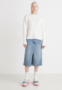 Hvit kabelstrikket genser med diagonale mønstre, kombinert med et denim midi-skjørt med slisse foran, og chunky sneakers med rosa såler.