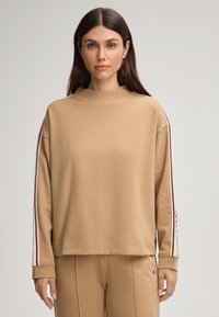 Felpa oversize color beige con collo alto, strisce a contrasto maroon e bianche sulle maniche e polsini a coste. Tessuto morbido e strutturato.