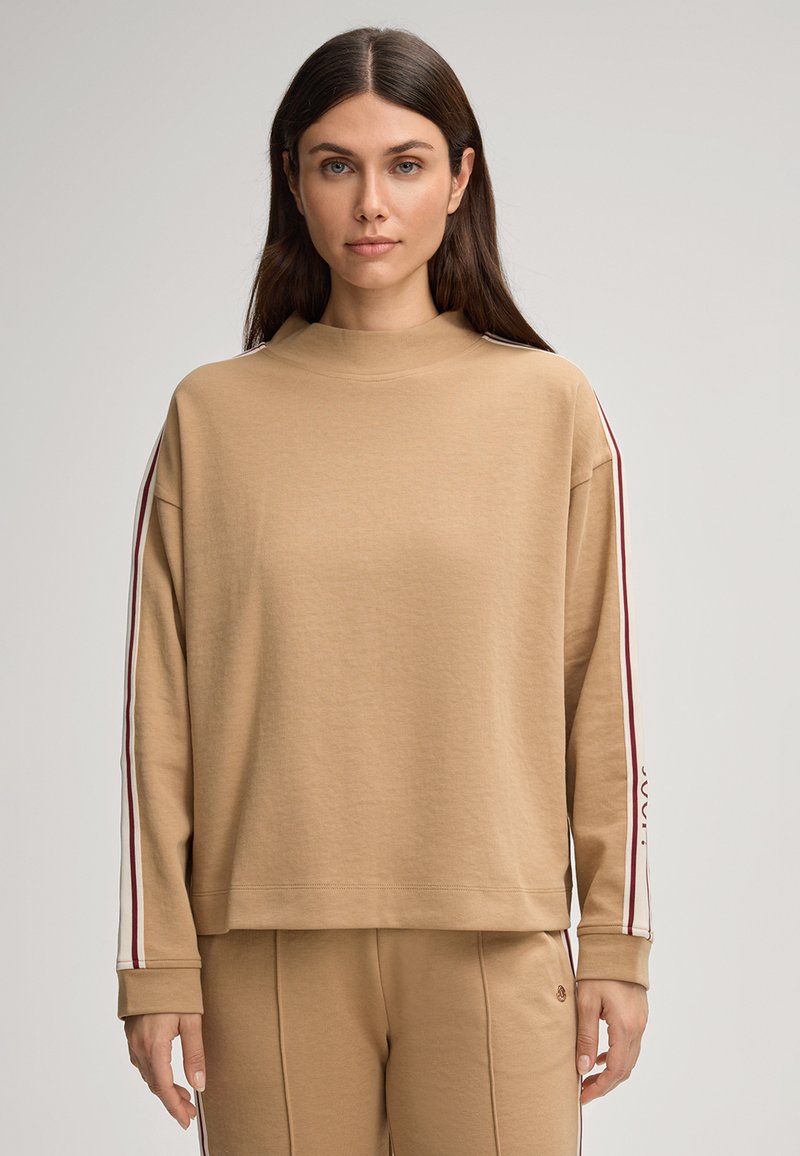 Felpa oversize color beige con collo alto, strisce a contrasto maroon e bianche sulle maniche e polsini a coste. Tessuto morbido e strutturato.