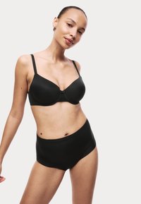 Reggiseno nero con coppe in schiuma e spalline regolabili, abbinato a mutandine nere a vita alta senza cuciture, entrambi caratterizzati da un tessuto morbido e da un design minimalista.