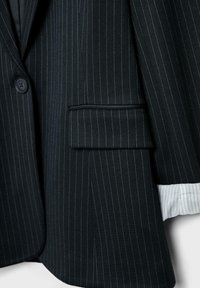 Schwarzer Nadelstreifen-Blazer mit einem Knopf, gekerbtem Revers und einer Brusttasche. Darunter ist ein hellblau gefüttertes Hemd zu sehen.