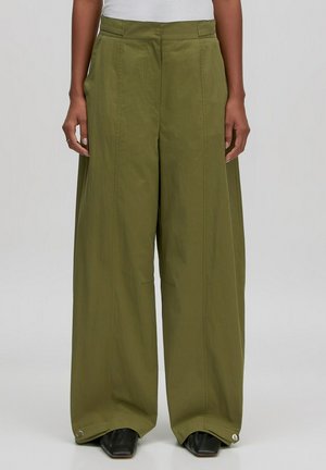 Olivengrüne weit geschnittene Hose mit hoher Taille, seitlichen Taschen und Knopfakzenten am Knöchel. Hergestellt aus leichtem Stoff.