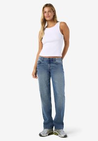 Λευκό ριμπ τοπ χωρίς μανίκια και μπλε φαρδιά τζιν παντελόνια, με κλασικό σχήμα και υφή. Γκρι αθλητικά παπούτσια με πράσινες λεπτομέρειες ολοκληρώνουν την εμφάνιση.